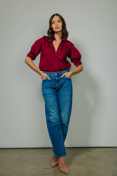 Woman wearing a red blouse and blue jeans against a plain background