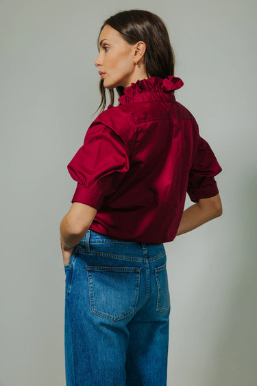 Woman wearing a red blouse and blue jeans against a gray background