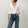 Woman wearing a white blouse and blue jeans against a plain background