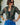 A woman wearing a vintage restructured men’s blouse in camo with white jeans on a neutral background.