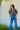 A woman wearing a vintage restructured men’s blouse in camo with white jeans on a neutral background.