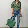 A woman wearing a restructured vintage men’s blouse in olive with a frill collar and blue jeans on a neutral background.