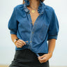 Woman wearing a blue denim shirt and black pants against a plain background