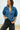 Woman wearing a blue denim shirt and black pants against a plain background