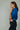 Woman wearing a blue shirt and dark jeans against a plain background
