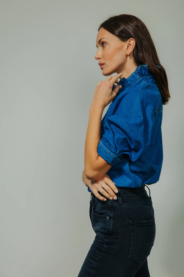 Woman wearing a blue shirt and dark jeans against a plain background