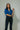 Woman wearing a blue denim shirt and black jeans against a plain background