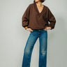 A woman wearing v-neck chocolate sweater and blue jeans and leopard print heels on a neutral background.