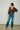 A woman wearing v-neck chocolate sweater and blue jeans and leopard print heels on a neutral background.