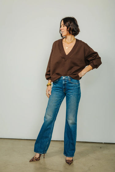 A woman wearing v-neck chocolate sweater and blue jeans and leopard print heels on a neutral background.