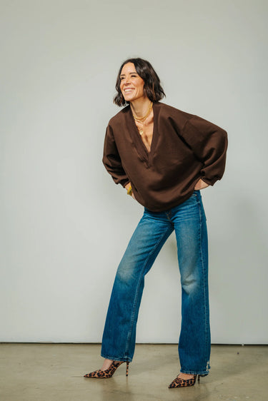 A woman wearing v-neck chocolate sweater and blue jeans and leopard print heels on a neutral background.