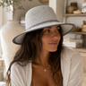 Woman wearing a straw hat in a cozy indoor setting with plants and shelves.