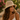 Woman wearing a straw hat and white top in a natural setting with flowers and greenery.