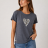 A woman wearing a dark gray heathered t-shirt with a white and black leopard-print heart graphic on the chest, paired with blue jeans, against a light gray studio background