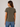A woman shown from the back wearing a short-sleeve crewneck t-shirt in olive green, paired with blue jeans, against a plain light gray studio background.