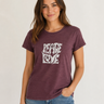 A woman wearing a heathered dark plum crewneck t-shirt with a distressed white 'PEACE LOVE' graphic on the front, paired with blue jeans, against a light gray studio background.