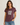 A woman wearing a heathered dark plum crewneck t-shirt with a distressed white 'PEACE LOVE' graphic on the front, paired with blue jeans, against a light gray studio background.