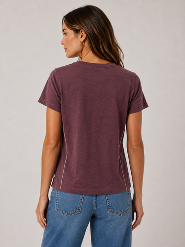 A woman shown from the back wearing a short-sleeve crewneck t-shirt in a heathered plum-brown color, paired with blue jeans, against a neutral light gray background.