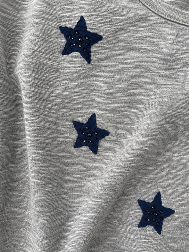 Close-up of a heather gray fabric garment with three dark navy blue embroidered star patches, each decorated with small rhinestones.