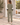 A woman viewed from behind wearing an olive green matching lounge set with white star details and striped sleeve accents, standing outdoors on a stone patio.