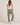A woman viewed from behind wearing olive green jogger sweatpants with embroidered white stars down the side and a brown star patch on the back pocket, paired with a white tank top and white sneakers against a light beige studio background.