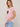 A woman wearing a light pink short-sleeve t-shirt with a sequined green heart graphic on the front, paired with light blue jeans, against a neutral beige background.