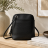 Black leather handbag on a wooden surface with books and a plant in the background