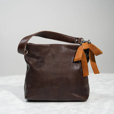 Brown leather handbag with a brown ribbon on a light gray background