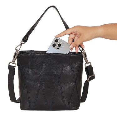 Black leather handbag with a hand reaching in to place a phone inside, on a white background