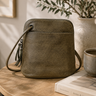 Miss green leather crossbody bag on a wooden table with a plant and books in the background