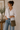 Woman wearing a white shirt and blue jeans, holding a green bag indoors.