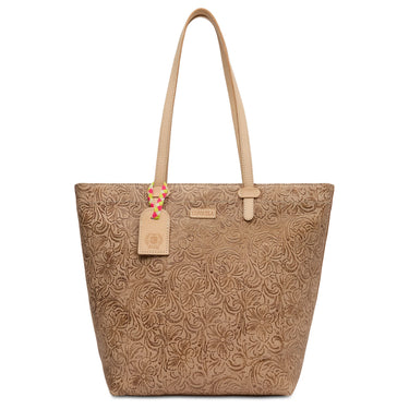 A tan leather tote bag with an embossed floral pattern, featuring dual shoulder straps, a small leather brand plaque, and a decorative hanging tag.