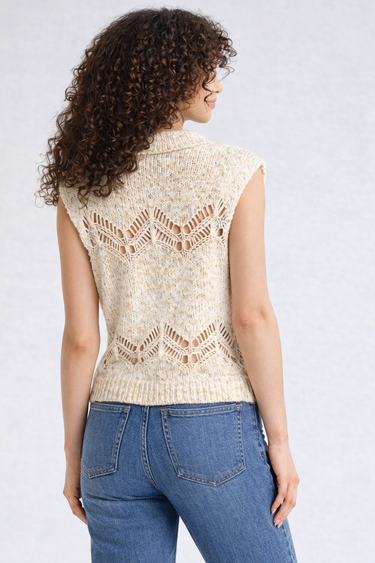 Woman wearing a beige sleeveless knitted top and blue jeans on a white background