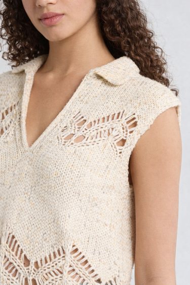 Close-up of a person wearing a beige sleeveless knitted top with intricate patterns.