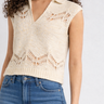 Woman wearing a beige sleeveless knitted top and blue jeans on a white background