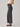 A side-profile view of a model wearing dark gray wide-leg cropped jeans, a white ribbed tank top, and black flat shoes against a light gray studio background.
