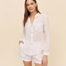 Woman wearing a white linen shirt and shorts on a beige background