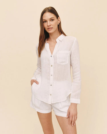 Woman wearing a white linen shirt and shorts on a beige background