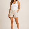 Woman wearing beige cargo shorts and a white tank top on a plain background