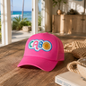 Pink cap with colorful logo on a wooden surface near a beach view