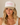 A woman wearing a beige and white trucker hat with pink text that reads 'Champagne PROBLEMS' against a warm beige background.