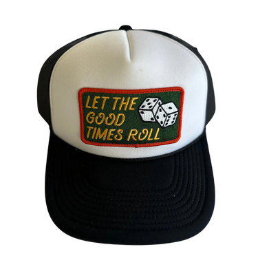 A black and white trucker hat with a rectangular embroidered patch on the front. The patch has a dark green background, yellow text reading 'LET THE GOOD TIMES ROLL', and two white dice with black dots.