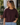 A woman wearing a burgundy sweatshirt with 3/4 sleeves and blue jeans outside a shop.