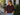 A woman wearing a burgundy sweatshirt with 3/4 sleeves and blue jeans outside a shop.