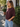 A woman wearing a burgundy sweatshirt with 3/4 sleeves and blue jeans outside a shop.