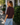 A woman wearing a burgundy sweatshirt with 3/4 sleeves and blue jeans outside a shop.