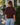 A woman wearing a burgundy sweatshirt with 3/4 sleeves and blue jeans outside a shop.