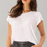 Woman wearing a white top and black pants against a gray background
