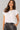 Woman wearing a white top and black pants against a gray background