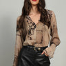 A woman wearing a v-neck chiffon printed brown blouse and black pants on a white background.